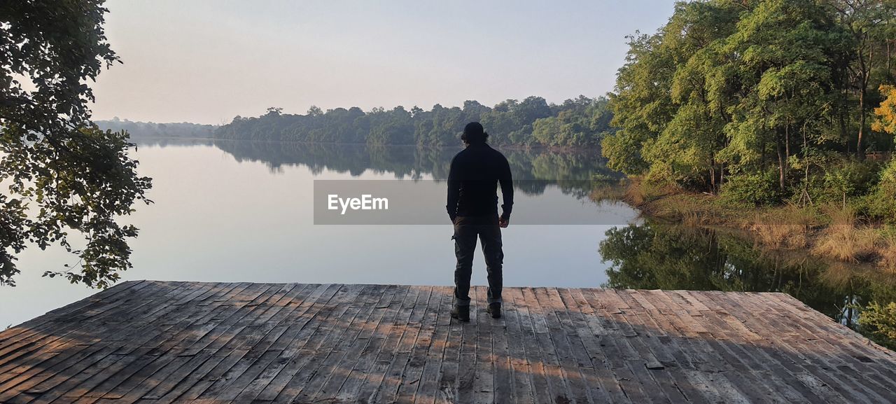 Rear view of man standing by lake against sky