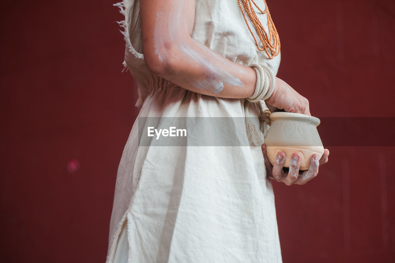 Midsection of woman with pot standing against wall