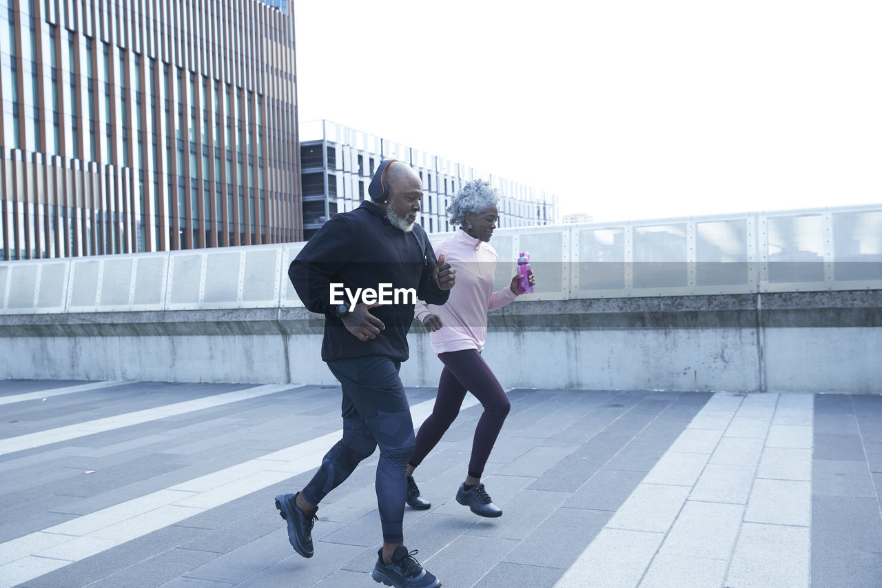 Man with headphones running by woman on footpath