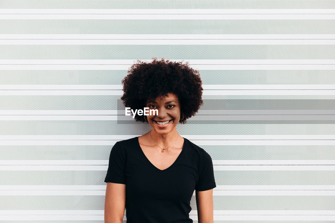 Afro woman laughing against a white wall. she is looking at camera and smiling.