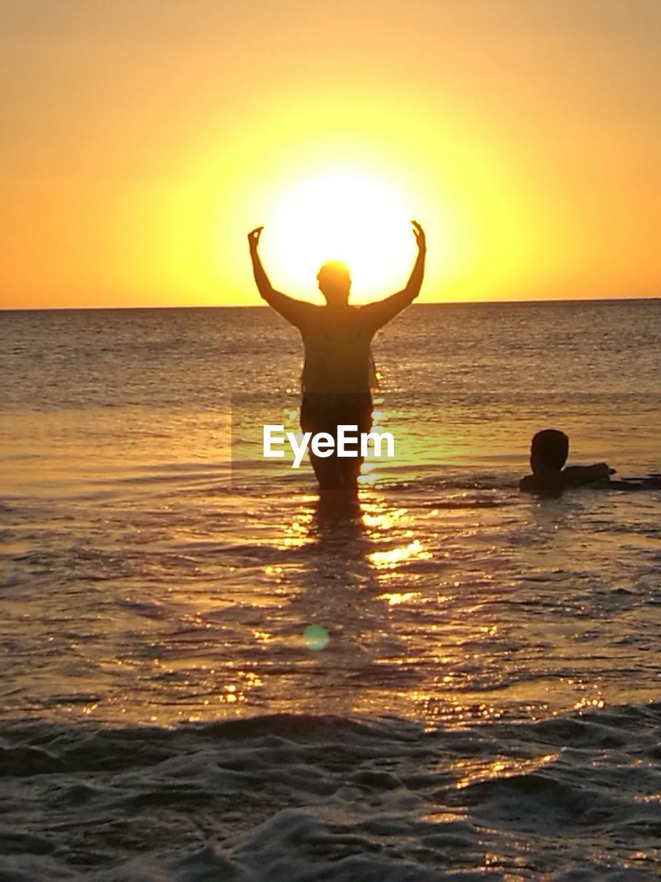 MAN STANDING ON BEACH AGAINST SUNSET SKY
