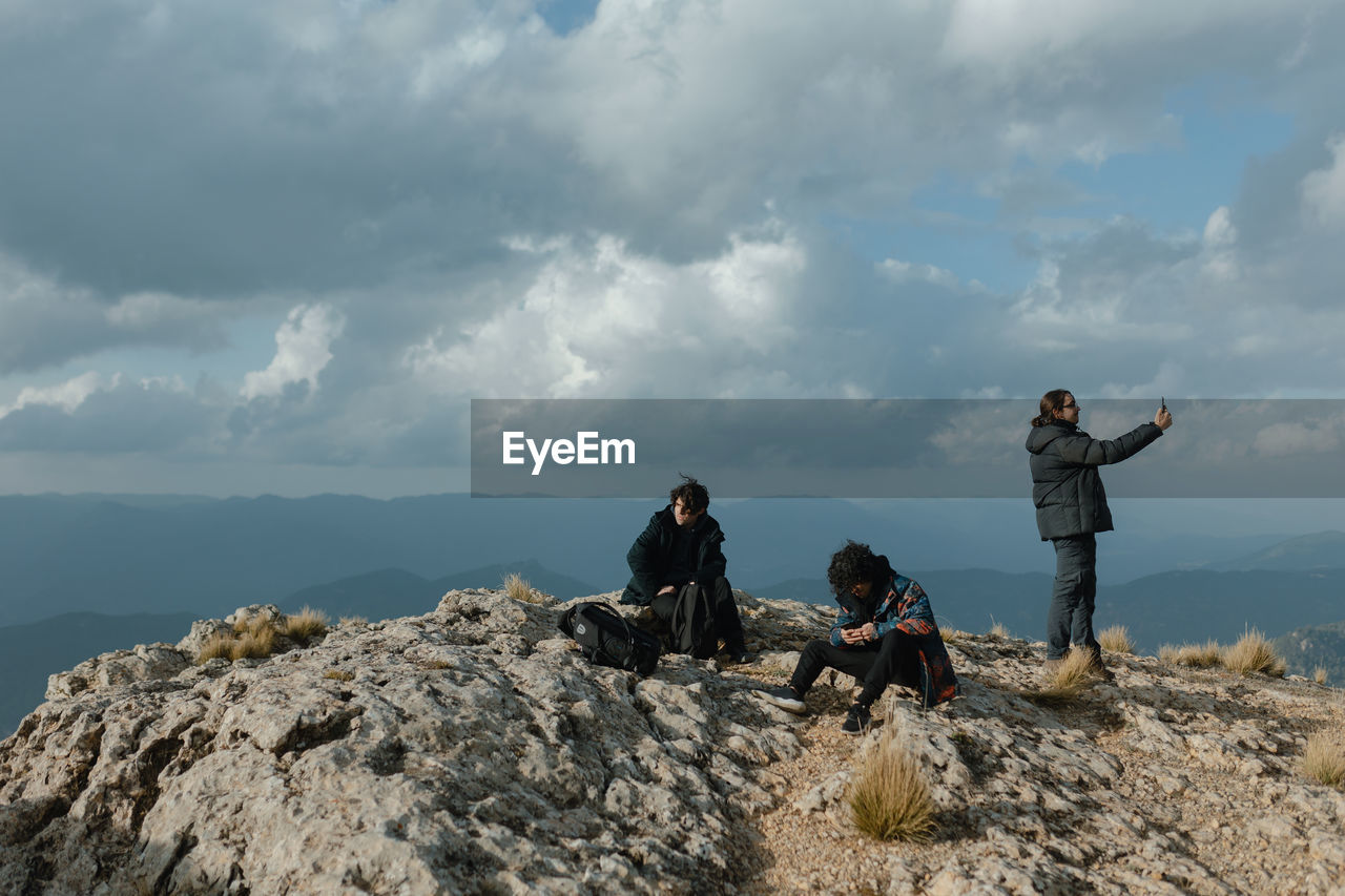 A group of hikers friends resting on top of a mountain peak with the mobile phones in their hands