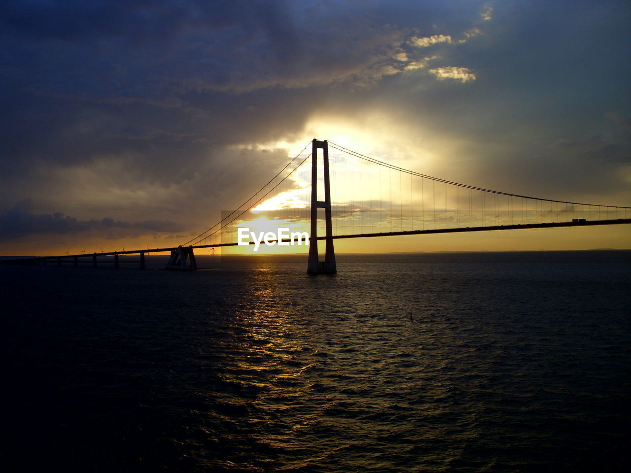 SILHOUETTE SUSPENSION BRIDGE OVER SEA AGAINST SKY DURING SUNSET