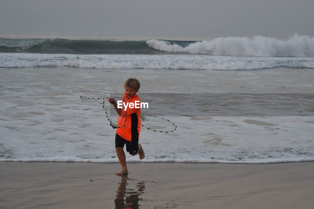 REAR VIEW OF BOY STANDING ON SHORE AT BEACH