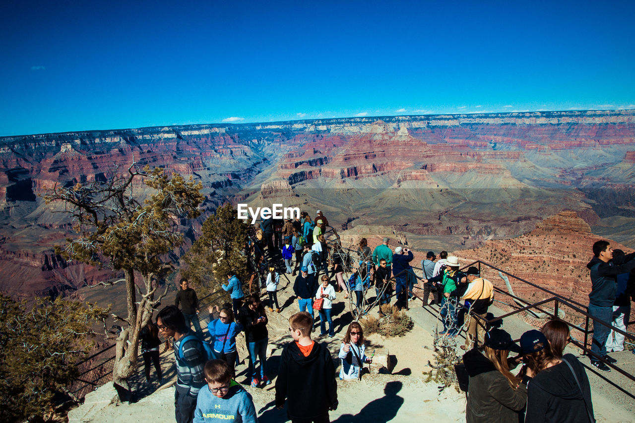 PEOPLE STANDING ON LANDSCAPE AGAINST MOUNTAIN