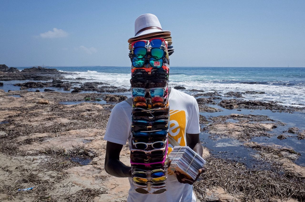 Man carrying stacks of sunglasses and hats