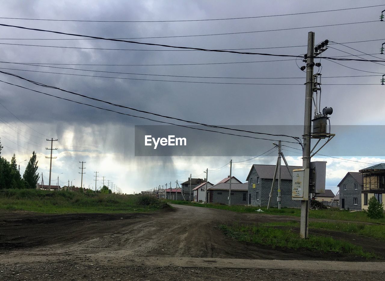 ROAD BY ELECTRICITY PYLON AND BUILDINGS AGAINST SKY