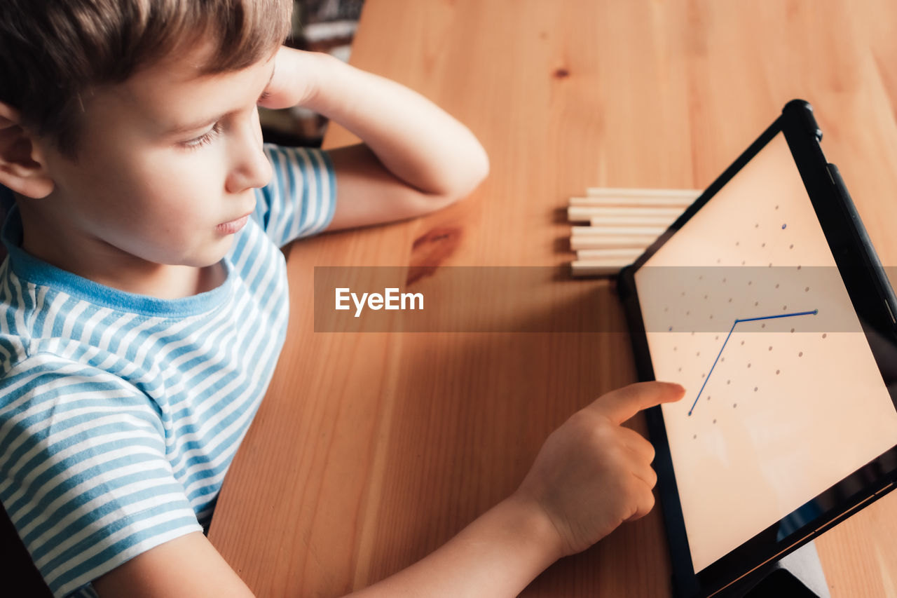 Modern child uses app on tablet to draw on tablet at home, distance learning