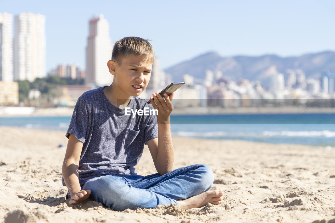 Teenager boy using a smart cell phone voice recognition function, send a voice message on city beach