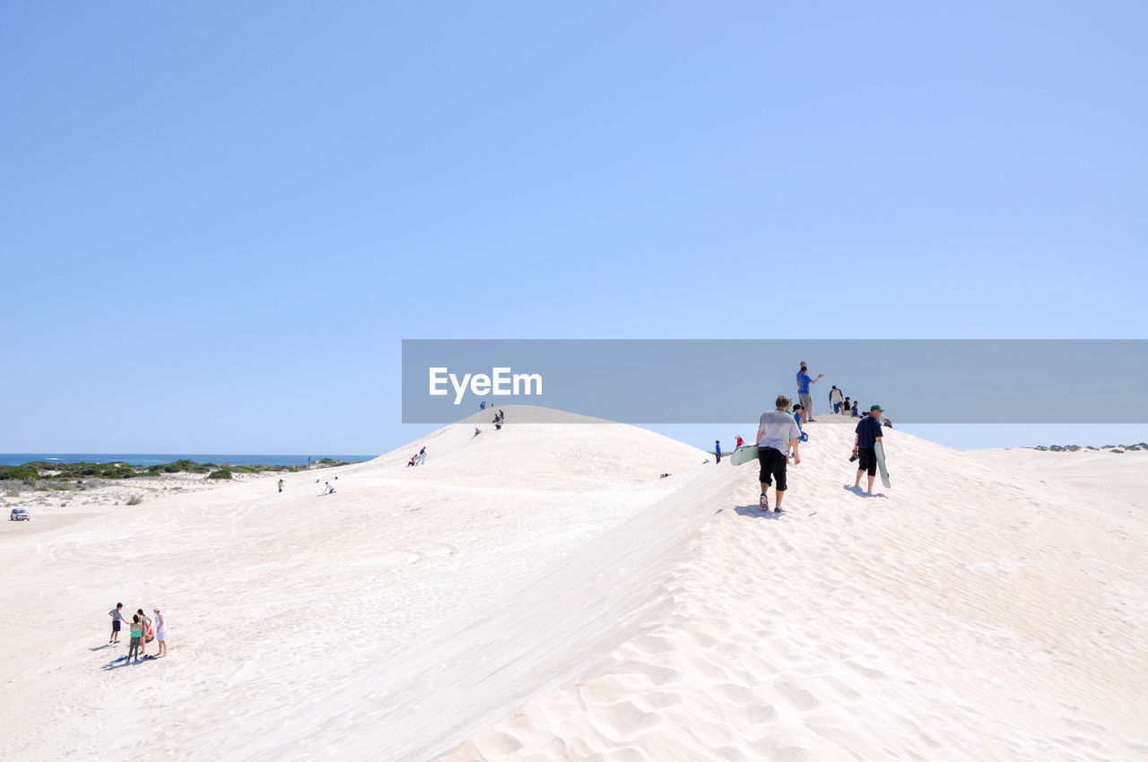 People at beach against clear blue sky