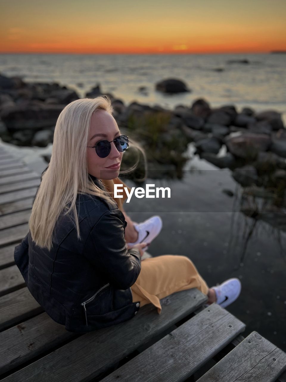 Portrait of young woman sitting at beach during sunset