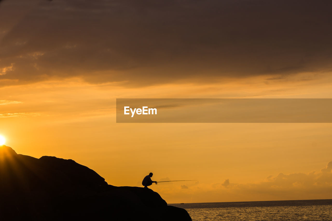 Silhouette person fishing at beach against sky during sunset