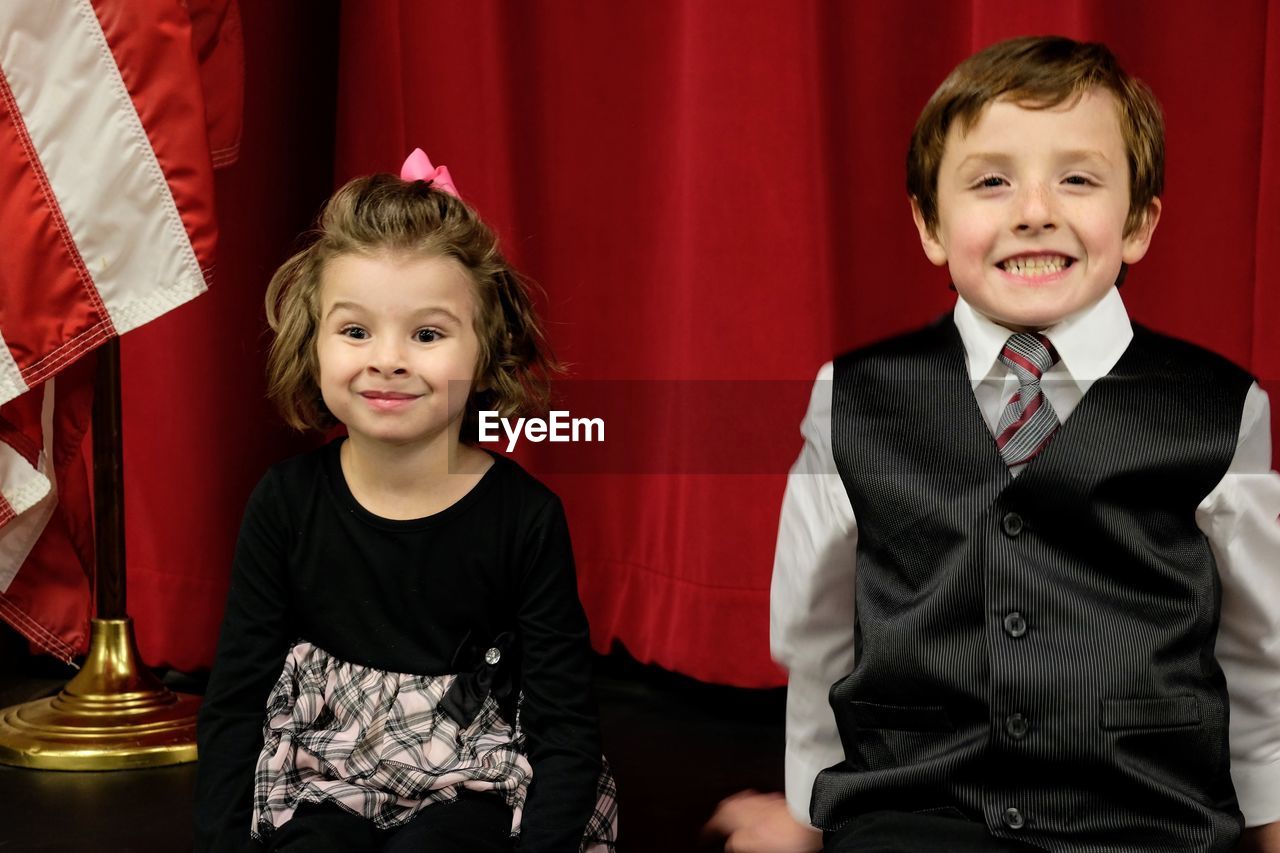 Smiling boy and girl making a face while standing against curtain