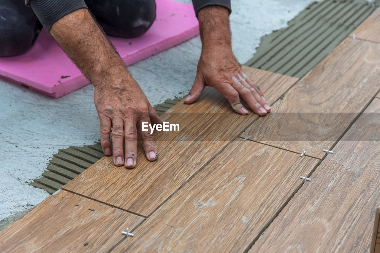 Worker placing ceramic floor tiles on adhesive surface, leveling