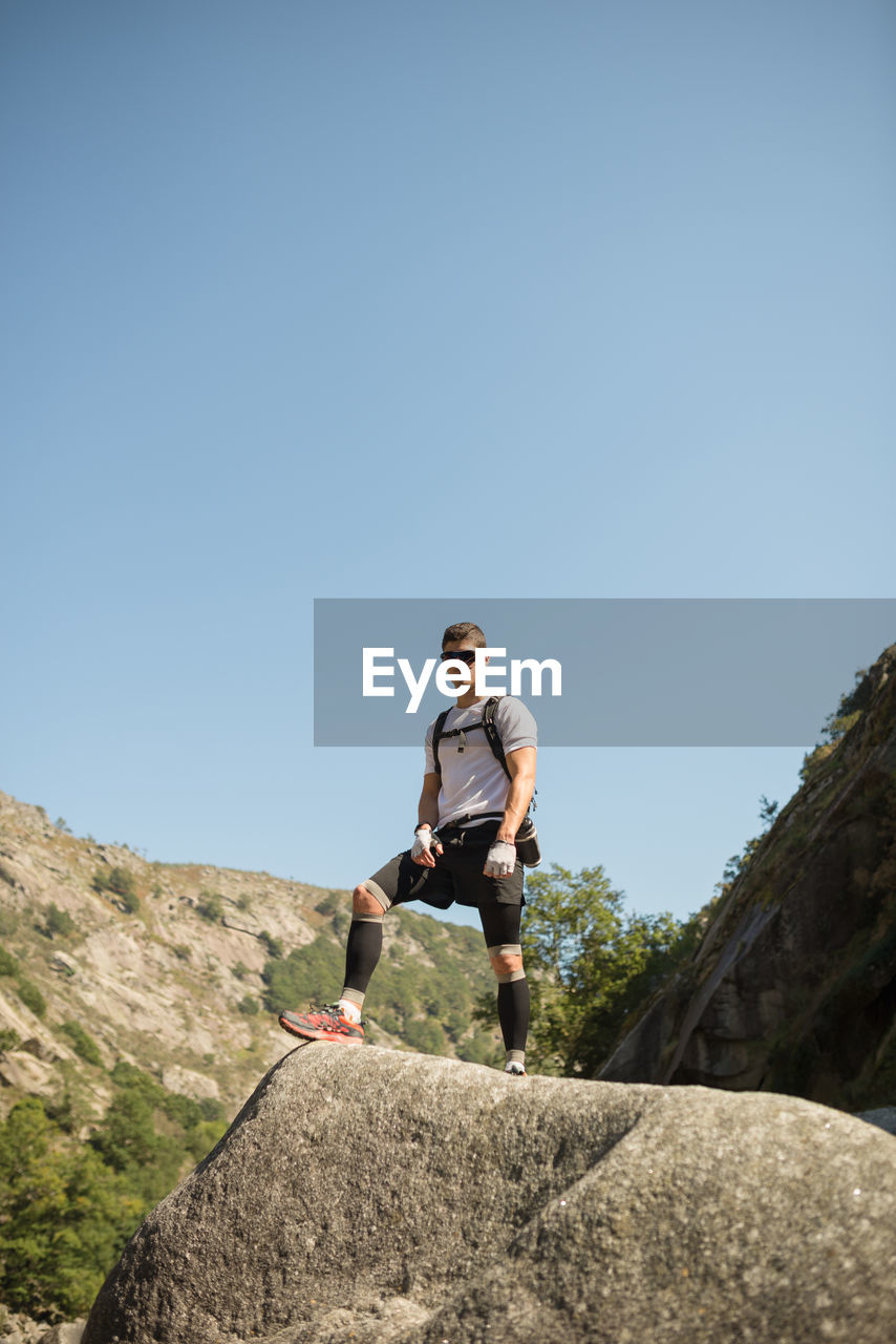 Low angle view of young man on rock against sky
