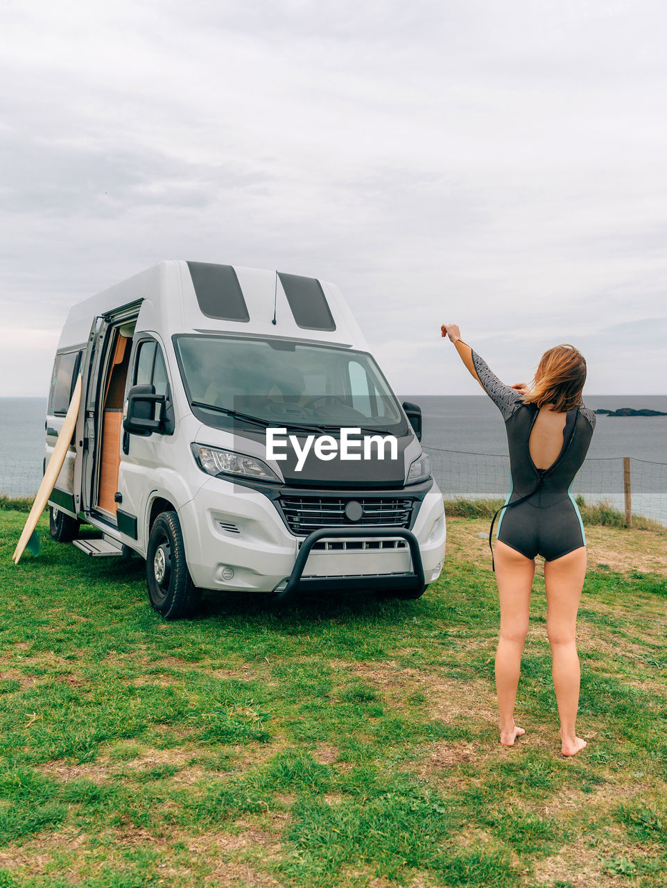 Young woman putting on her wetsuit for surfing next to her camper van