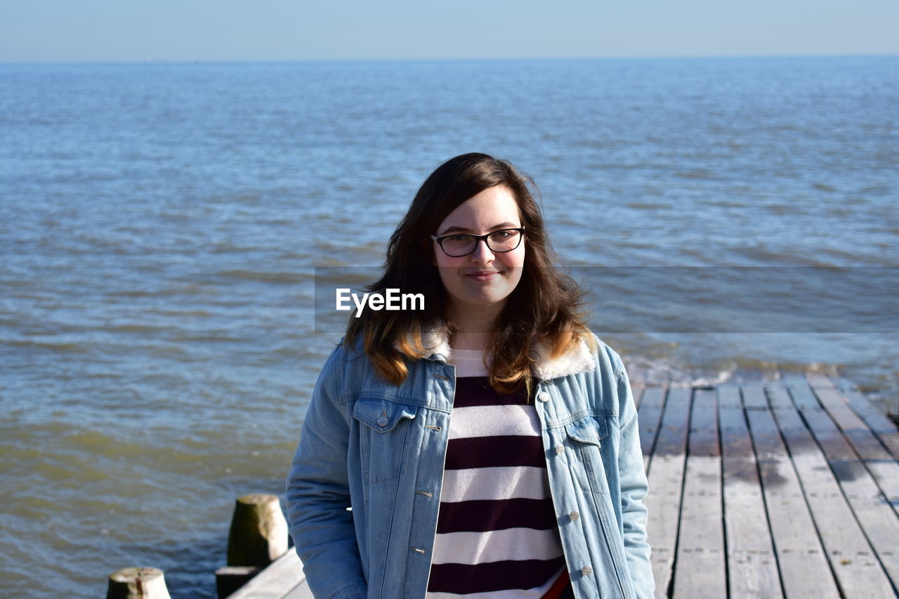 Portrait of smiling young woman standing against sea