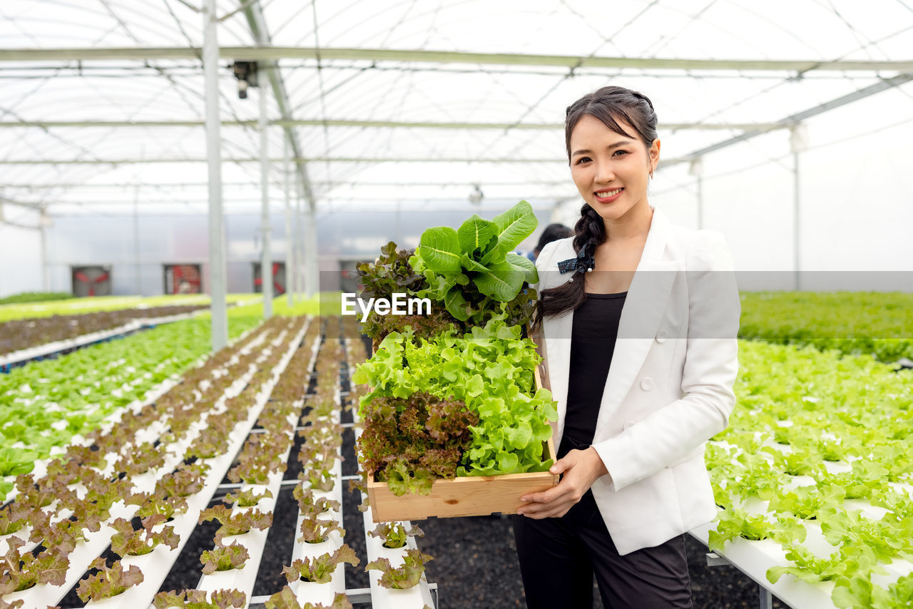 Portrait of smiling woman standing in greenhouse