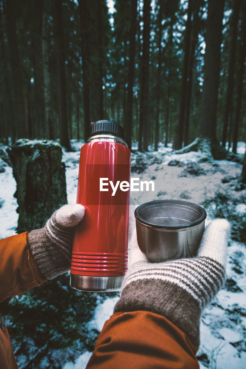 Cropped hands of woman having drink against trees in forest during winter