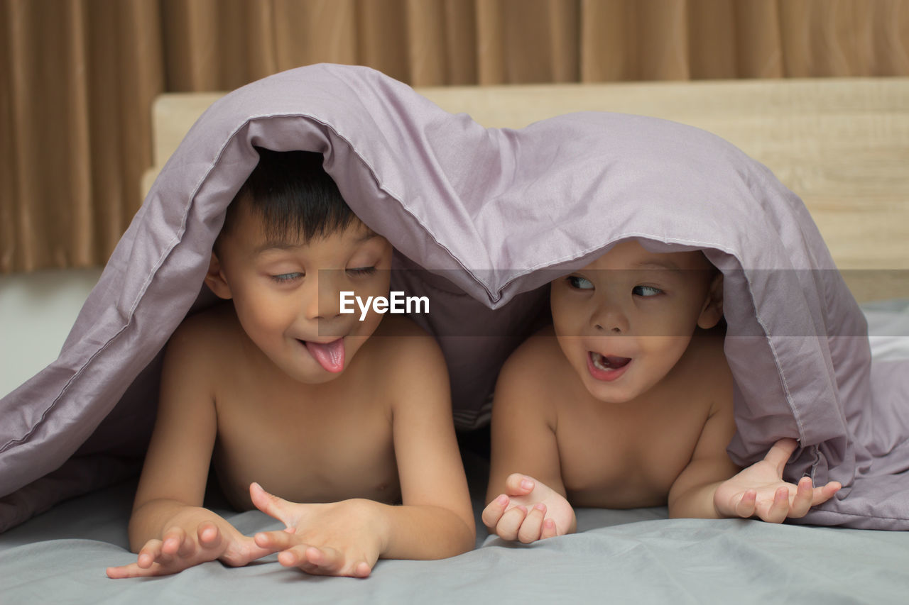 Cute playful siblings making face in bed at home