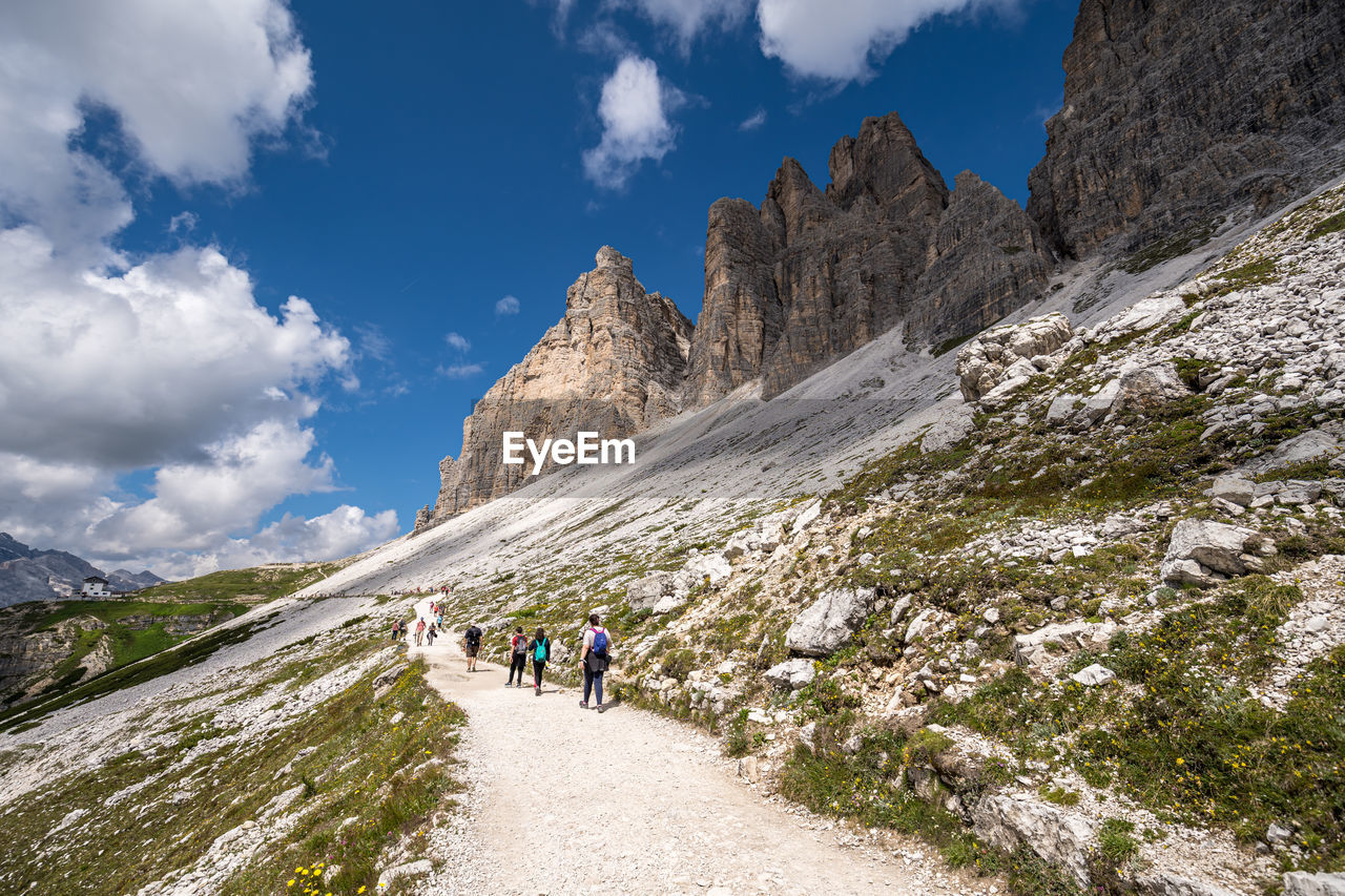 PEOPLE WALKING ON ROCKS AGAINST MOUNTAINS