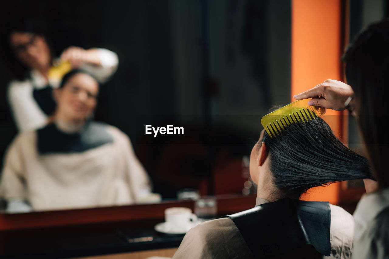 Hairdresser combing customer hair in salon