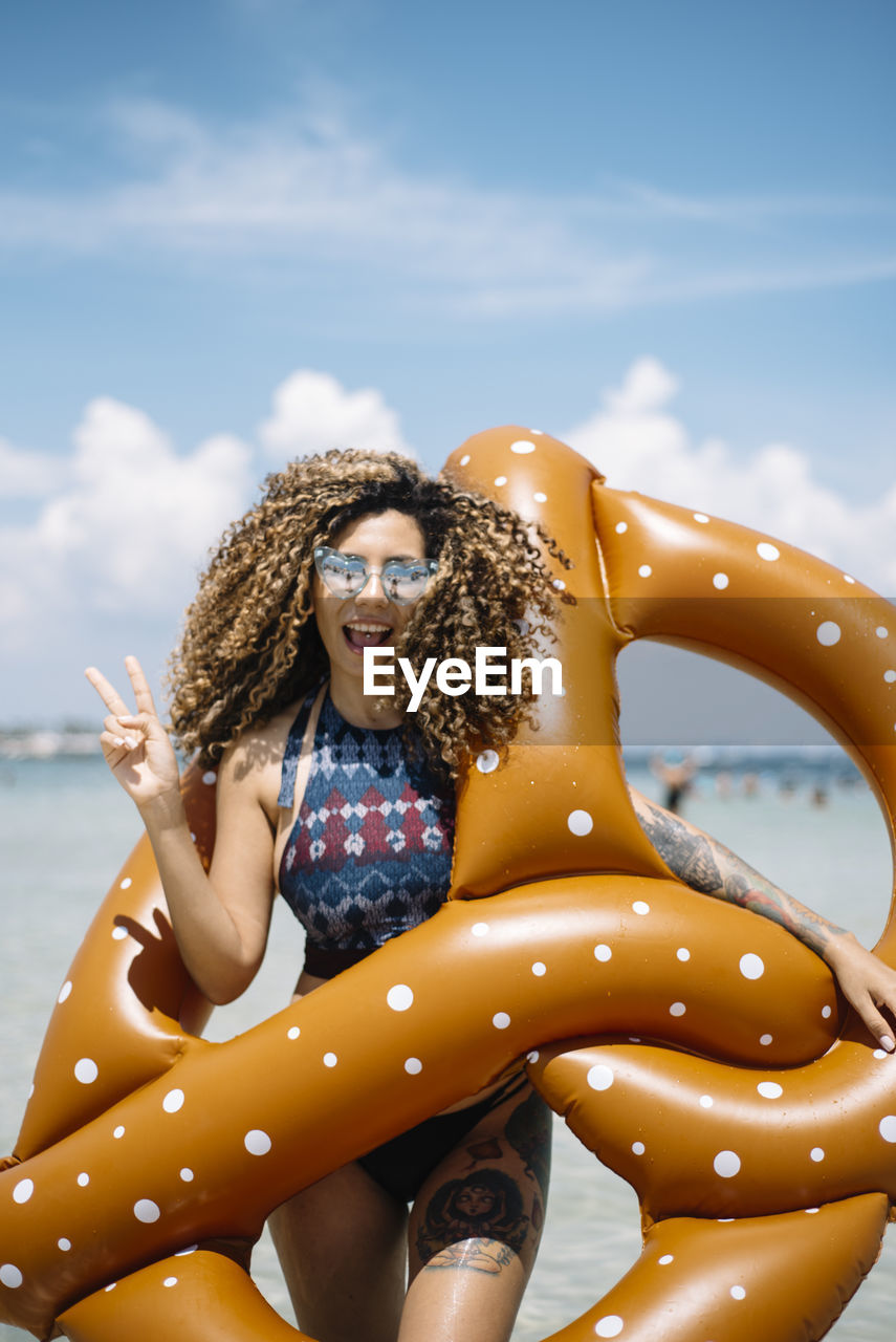 Portrait of smiling woman holding pool raft while standing at beach