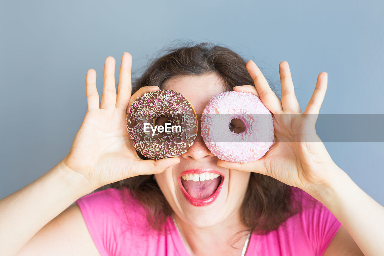 Cheerful woman holding donuts against wall