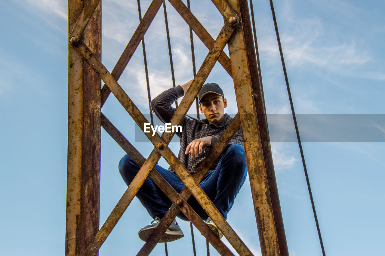 Full length portrait of teenage boy on rusty built structure against sky