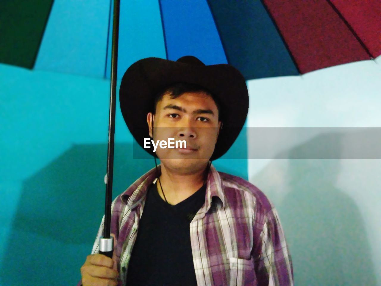 PORTRAIT OF YOUNG MAN WEARING HAT STANDING AGAINST BLUE BACKGROUND