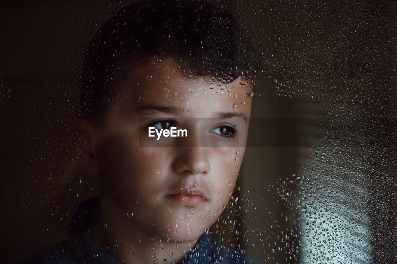 Thoughtful boy seen through wet glass