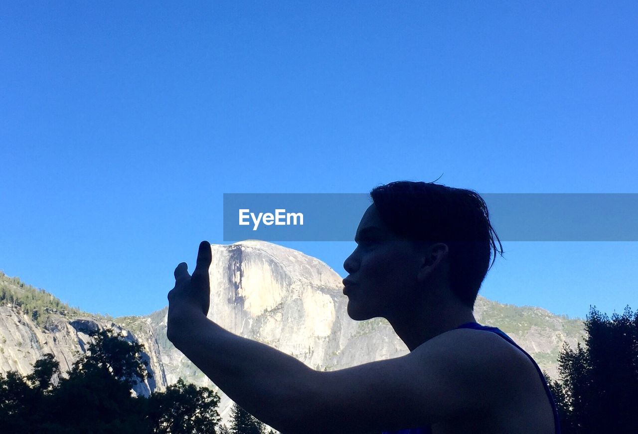 LOW ANGLE VIEW OF WOMAN STANDING ON MOUNTAIN AGAINST CLEAR BLUE SKY