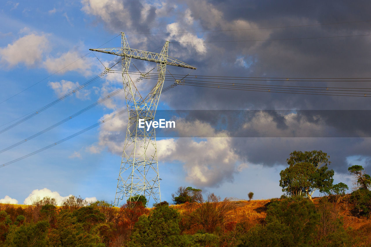Low angle view of electricity pylon on land against cloudy sky