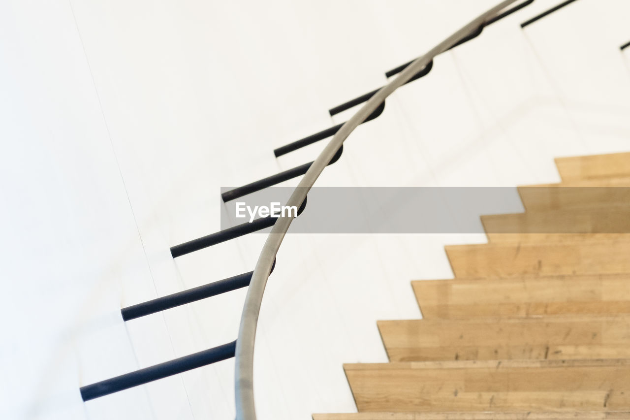 Metallic railing over wooden staircase by white wall