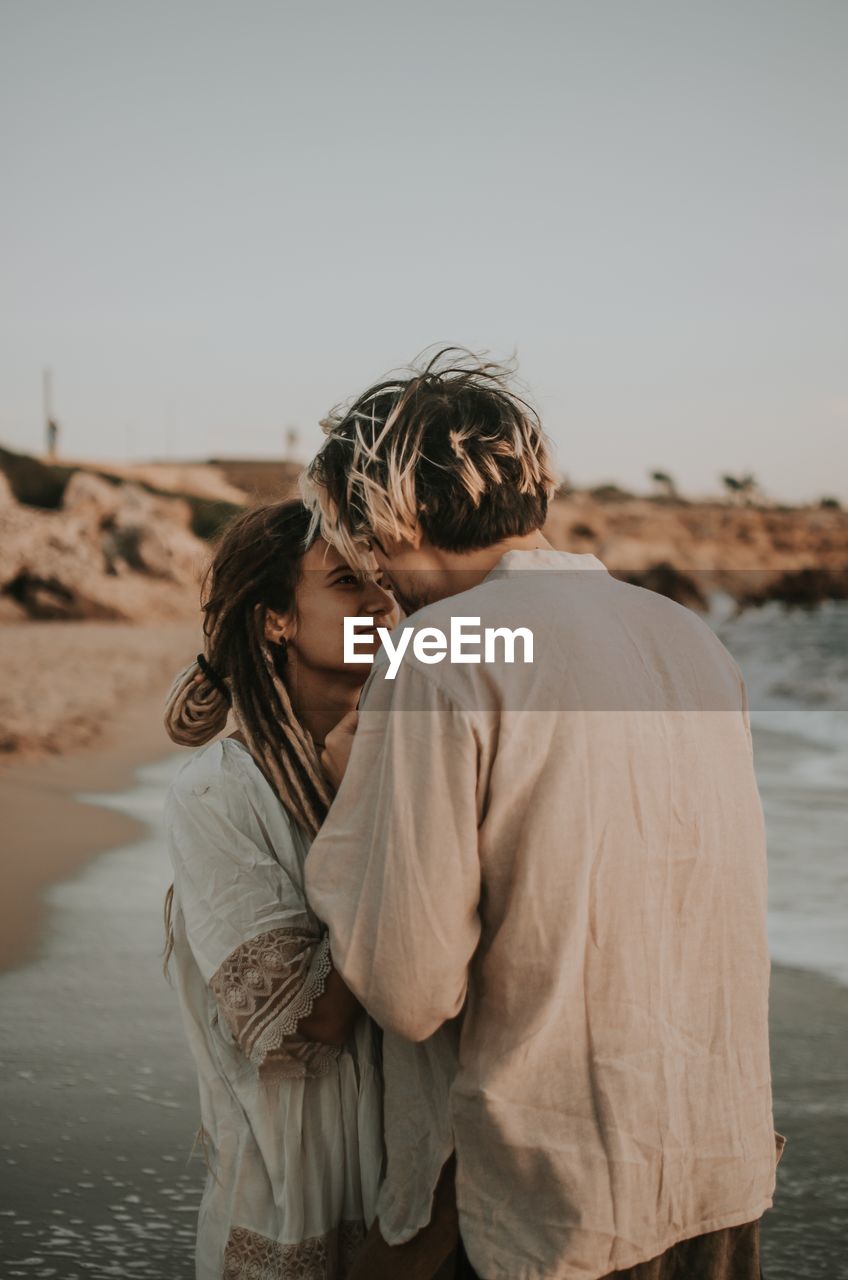 REAR VIEW OF COUPLE STANDING AT BEACH