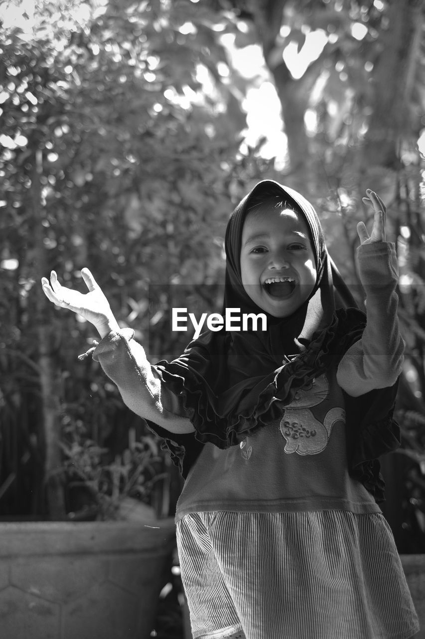 Portrait of cheerful girl wearing hijab while standing against plants