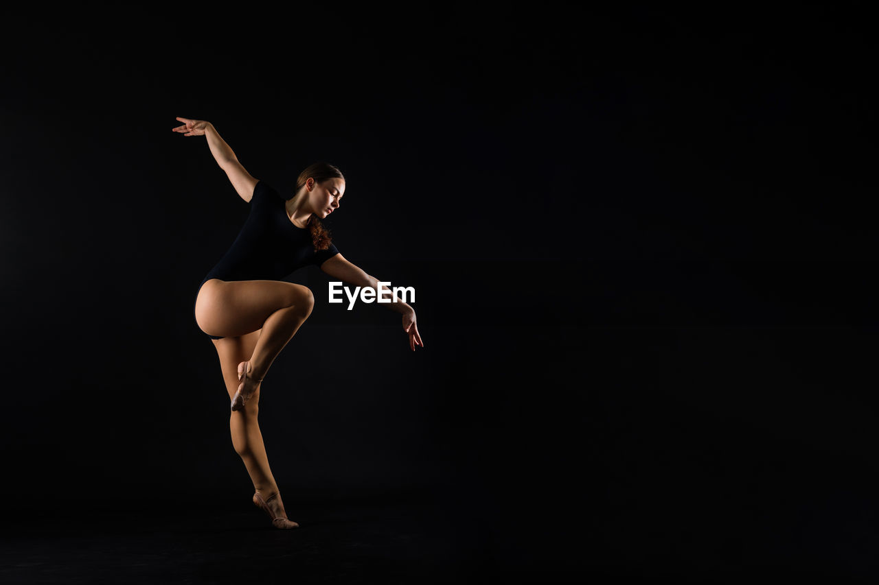 full length of young woman jumping against black background