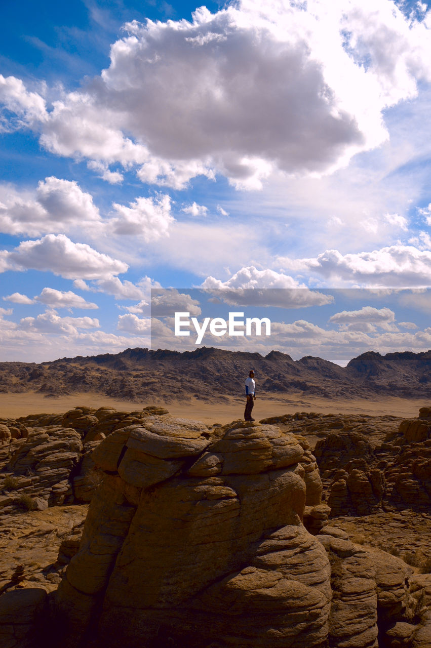 Man standing on rock formation against sky