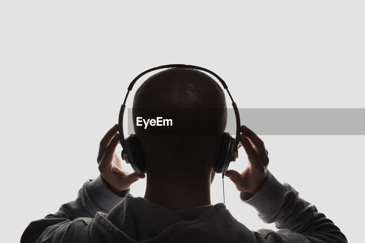 Rear view of man listening to music on headphones against white background