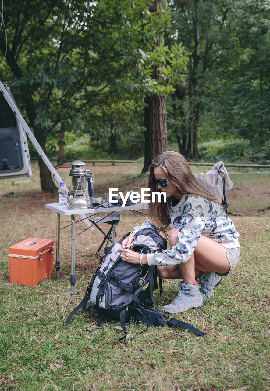 Woman packing backpack on field in forest