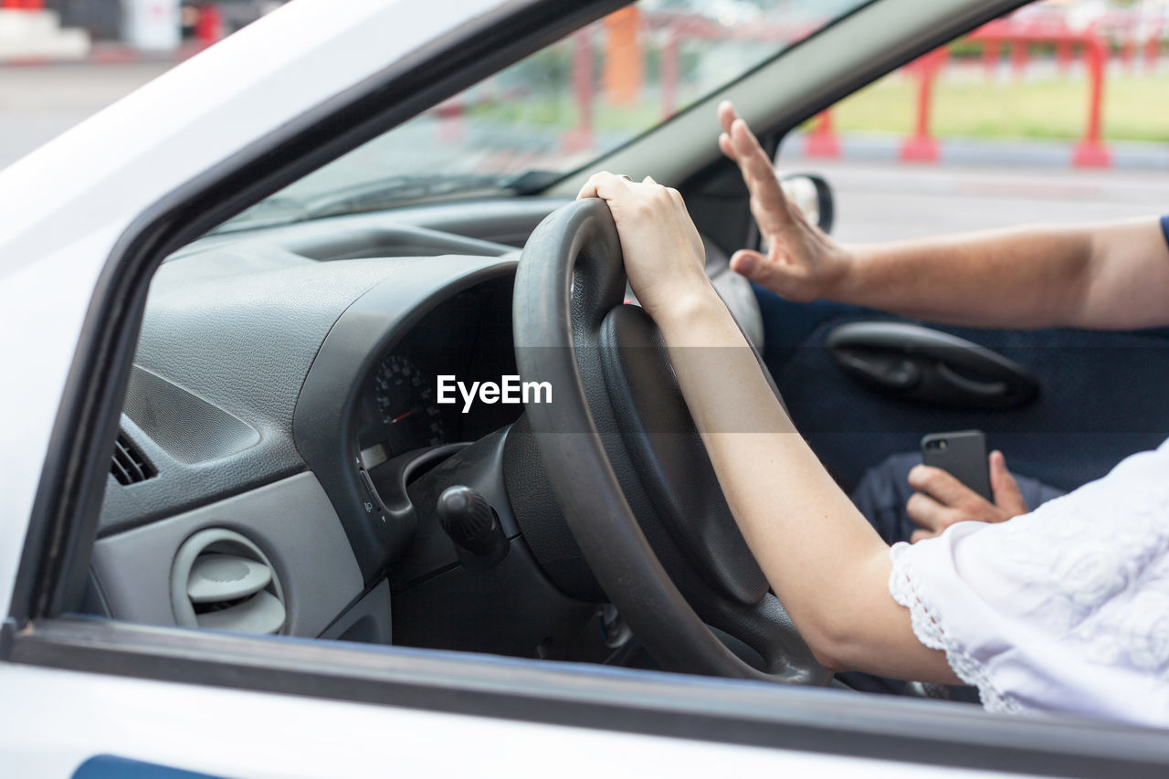 Cropped hand of woman driving car with man
