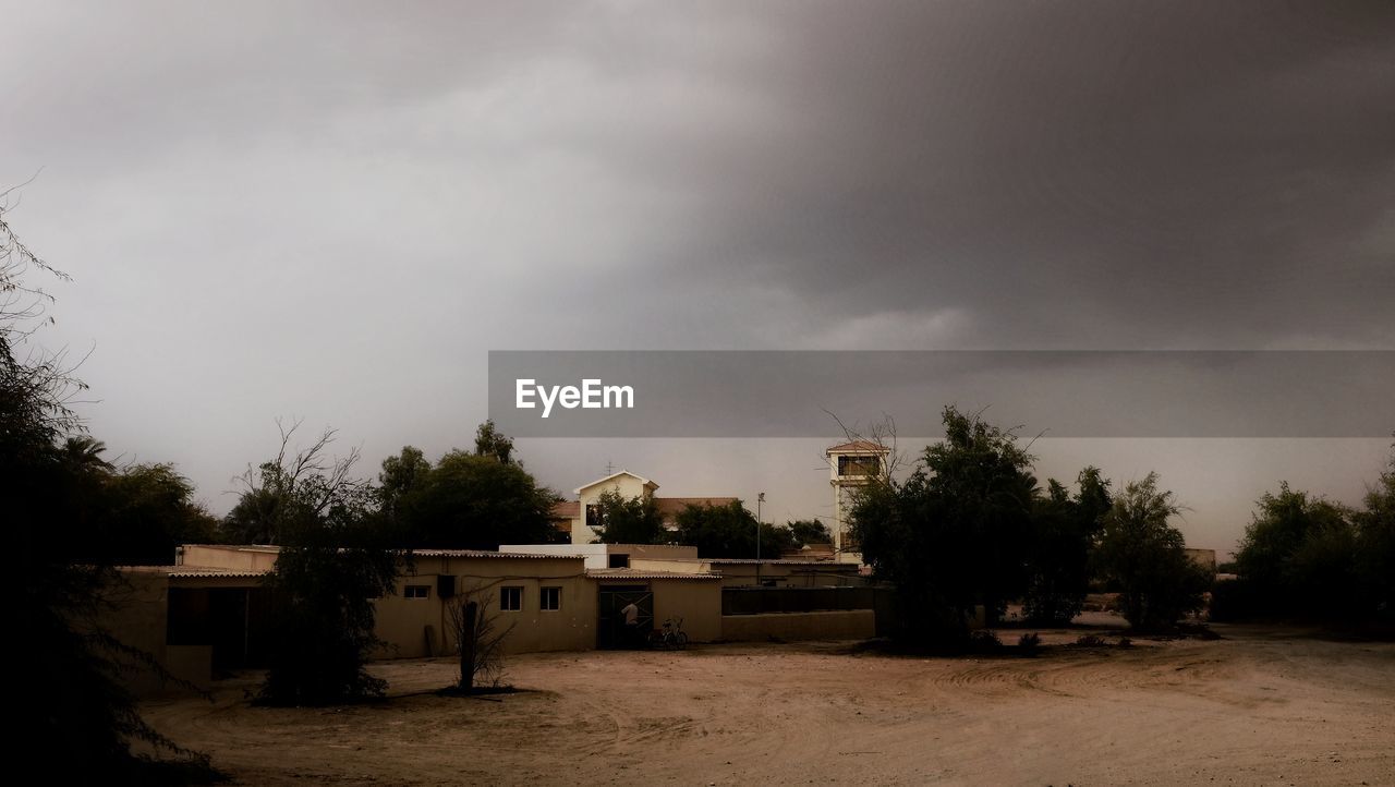 HOUSES BY TREES AGAINST STORM CLOUDS