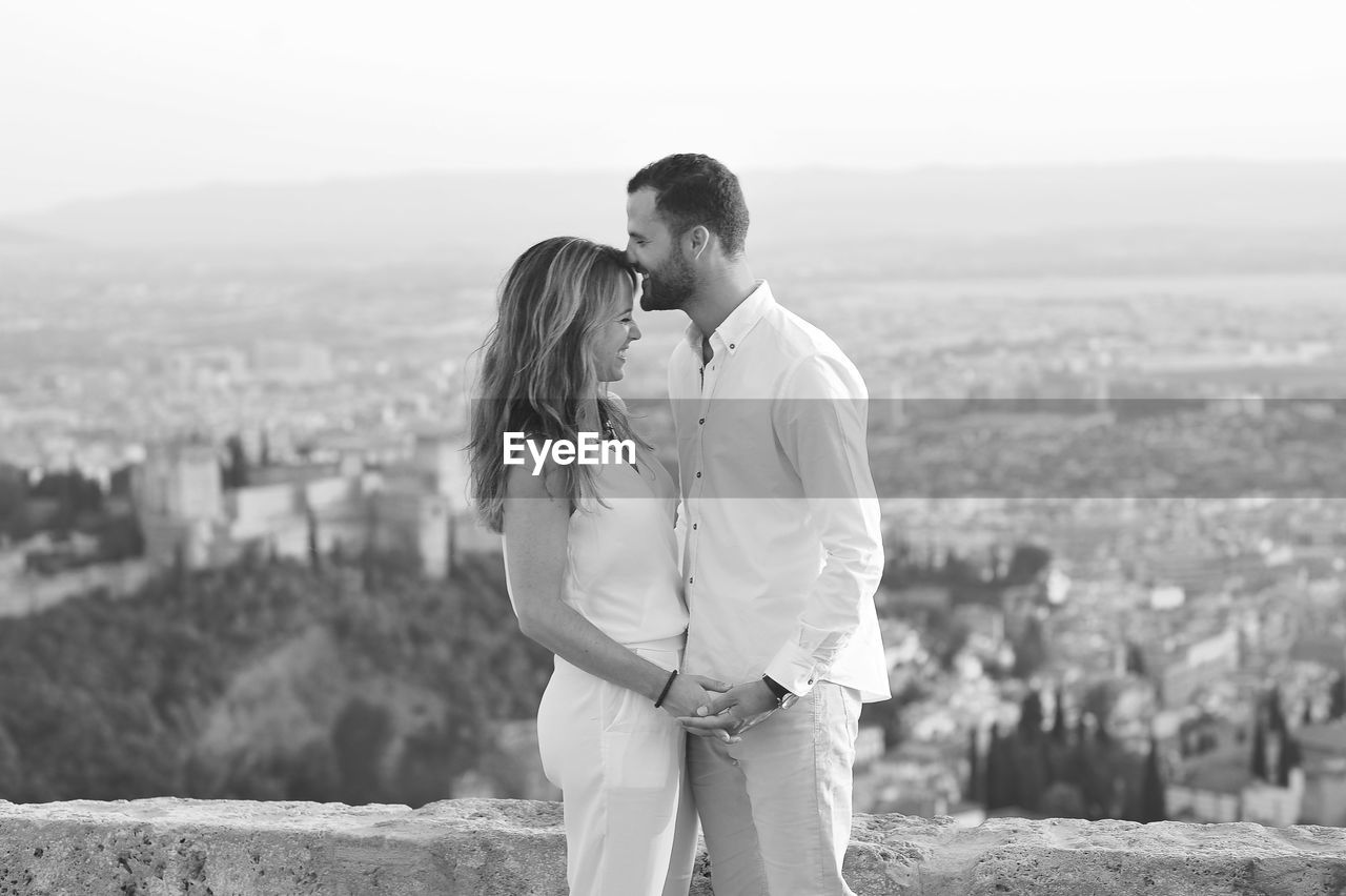 Side view of young romantic couple standing by retaining wall