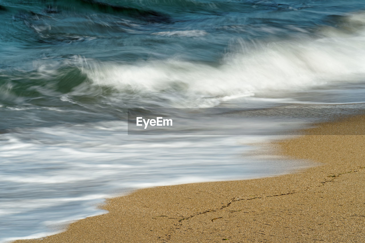 Detail view of a wave runs out on a beach, the blue color of the sky is reflected in the water