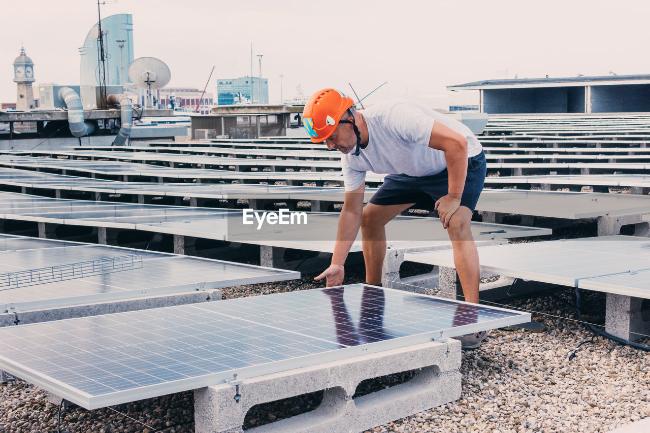 Serious male in helmet worker installing modern solar panels while working in industrial area of plant on sunny day