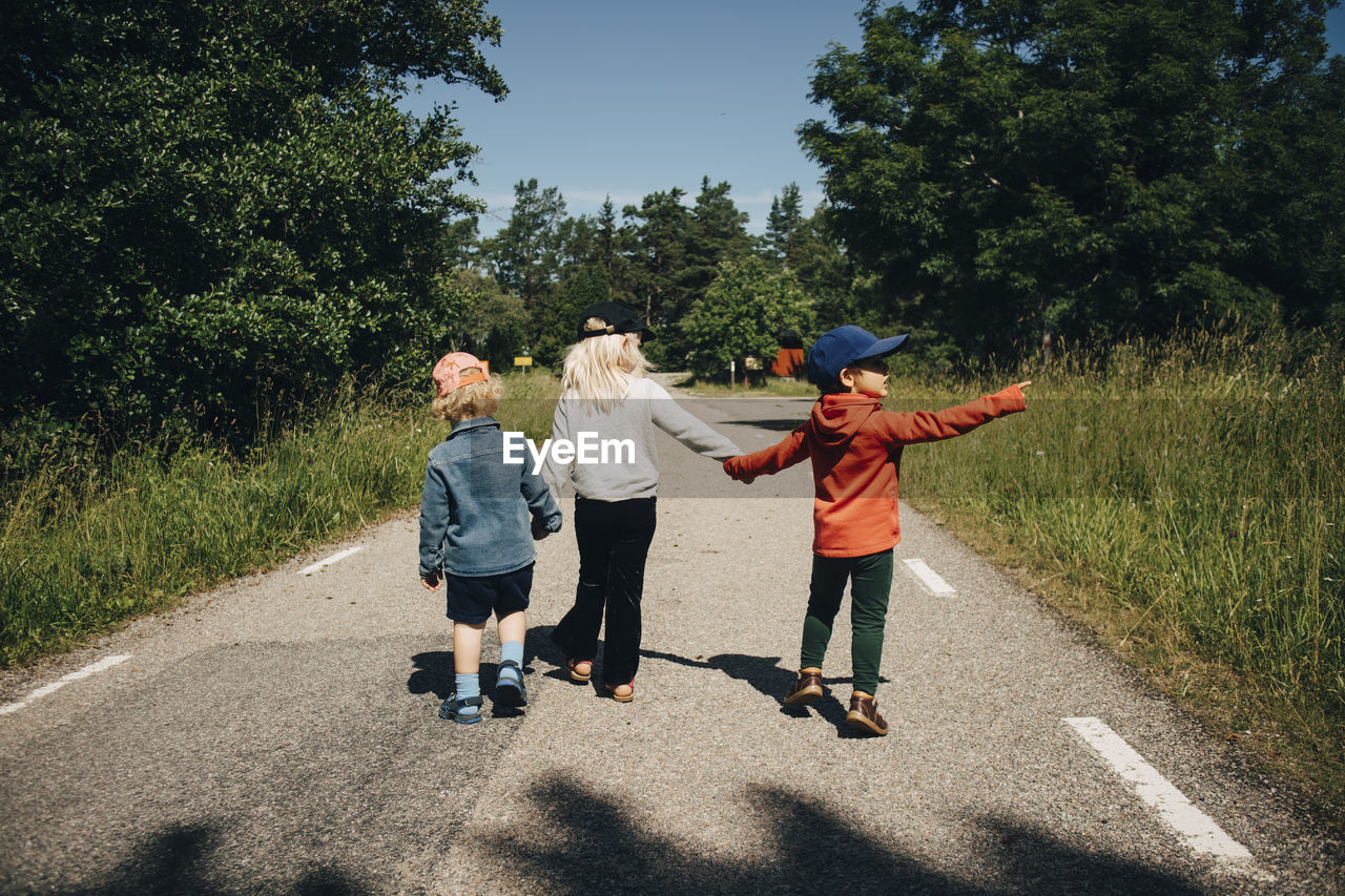 Rear view of sister with brothers walking on road during sunny day