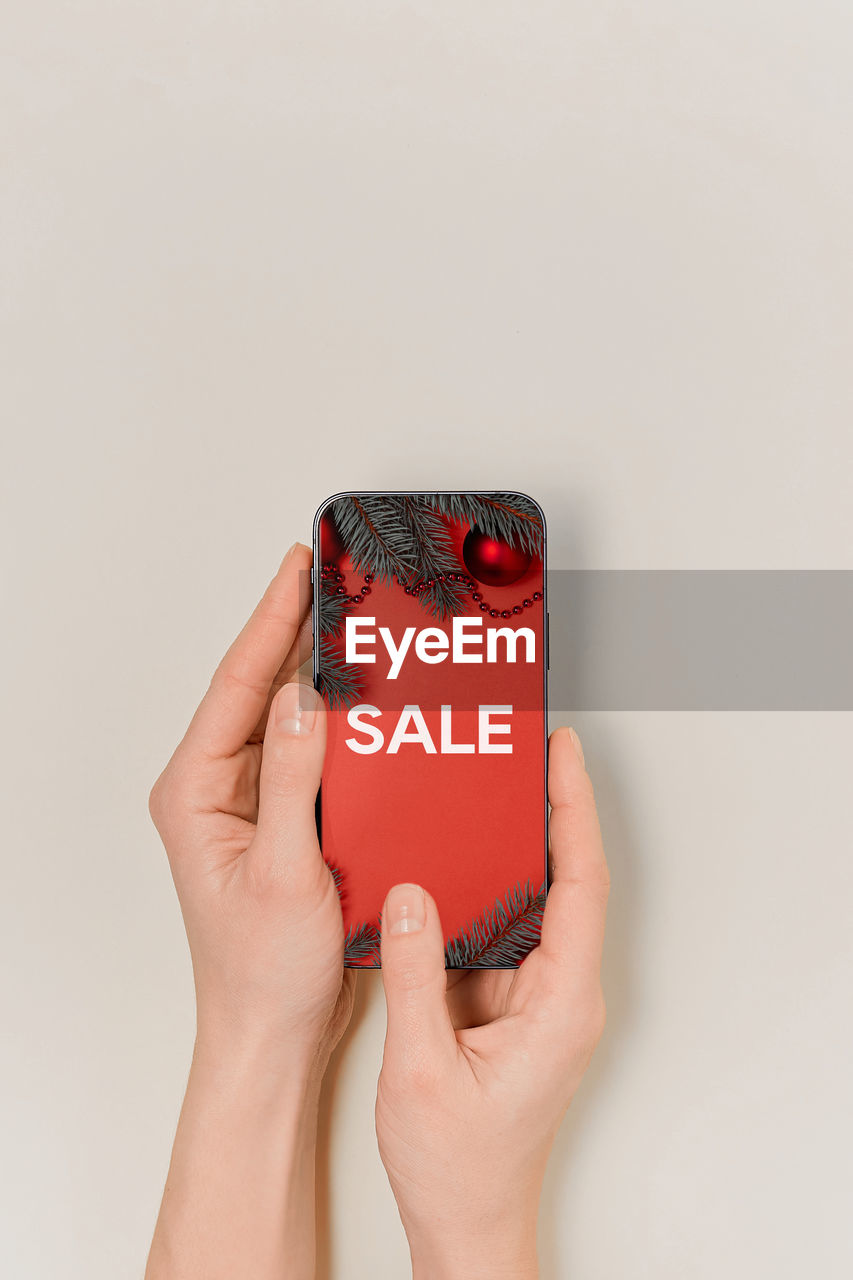 cropped hands of woman holding mobile phone against white background