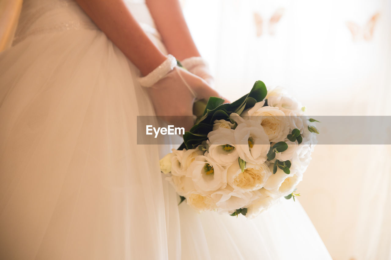 Midsection of bride wearing wedding dress while holding bouquet