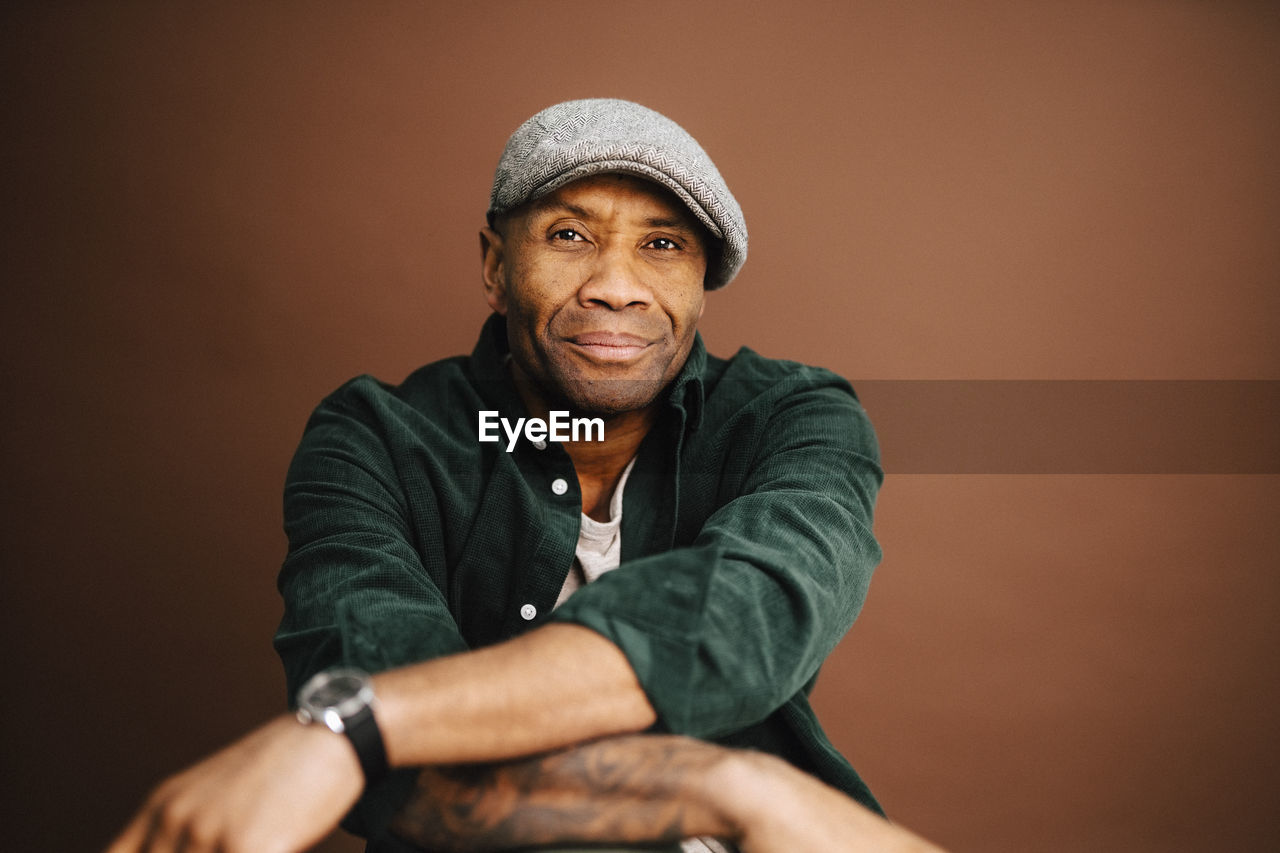 Portrait of mature man wearing beret over brown background in studio