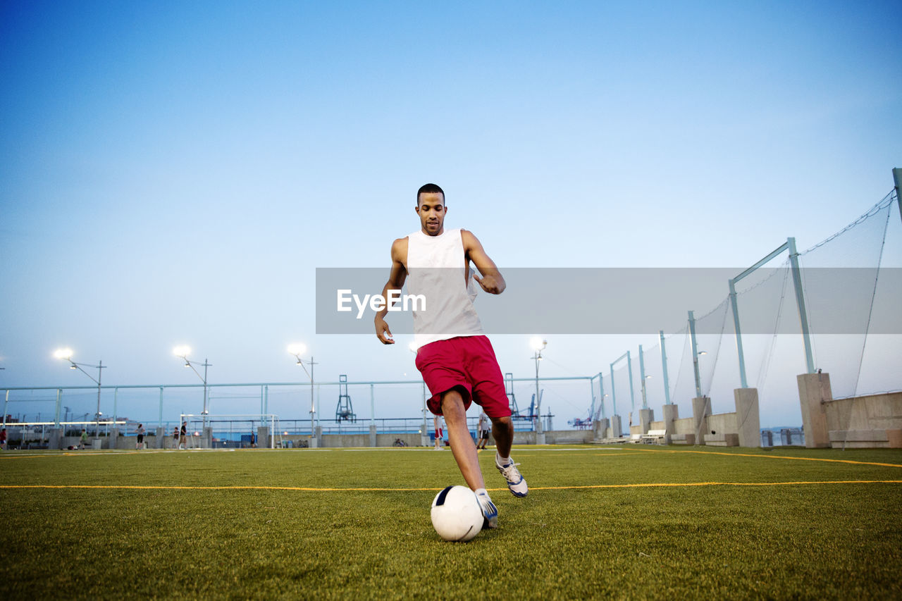 Young man playing soccer on field against clear sky